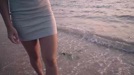 attractive woman in dress walks along surf line slow motion