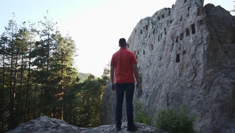 Tourist-standing-in-front-of-a-natural-rock-foramtion-and-a-sacrificial-altar-called-the-Eagle's-Rock,-or-more-commonly-known-as-Orlovi-Skali-located-in-the-Rhodope-Mountains-in-Bulgaria