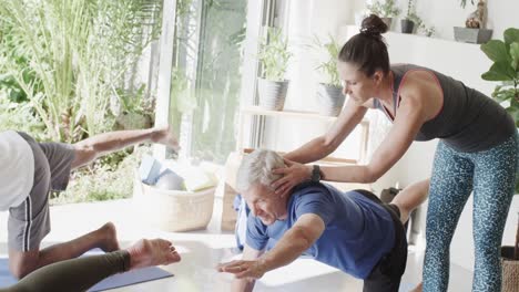 diverse seniors practicing pilates with female coach in sunny room, unaltered, in slow motion