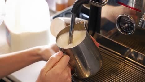 masked barista froths milk on commercial espresso machine, slow motion over the shoulder 4k