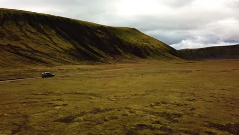 Aerial-landscape-view-over-a-four-wheel-drive-car-traveling-on-a-dirt-road-through-icelandic-highlands