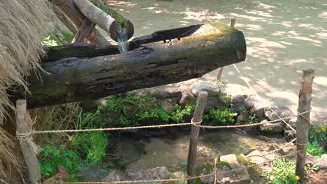 Water-flowing-through-open-wooden-pipes-filling-old-decrepit-wooden-beam-of-water-mill-for-milling-wheat-and-rice-in-Korean-folk-village-Yongin-City