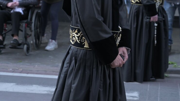 Penitente che indossa una tunica nera tradizionale e tiene in mano un rosario mentre cammina in una processione religiosa.