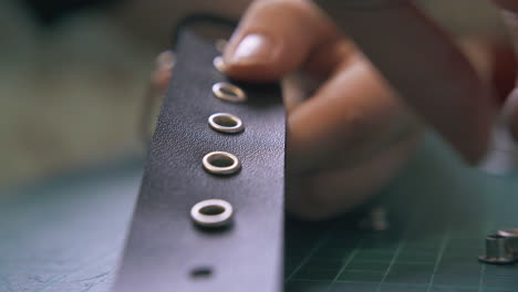 professional tailor puts black leather eyelets into belt