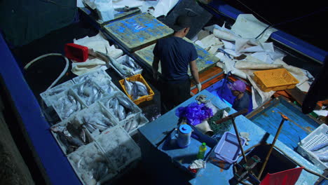 A-man-sorting-fresh-fish-in-tray-for-trading-in-fishing-boat-at-dawn,-tho-Quang,-Da-Nang-city,-Vietnam