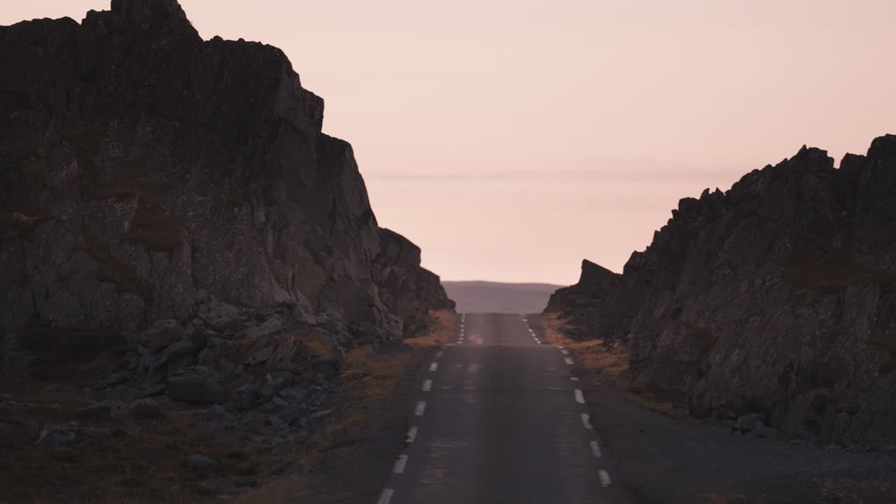 Driving on the narrow asphalt road along the rocky shores of the fjord in the warm light of the sunset