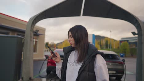 Woman-with-an-electirc-vehicle-charging-and-using-phone