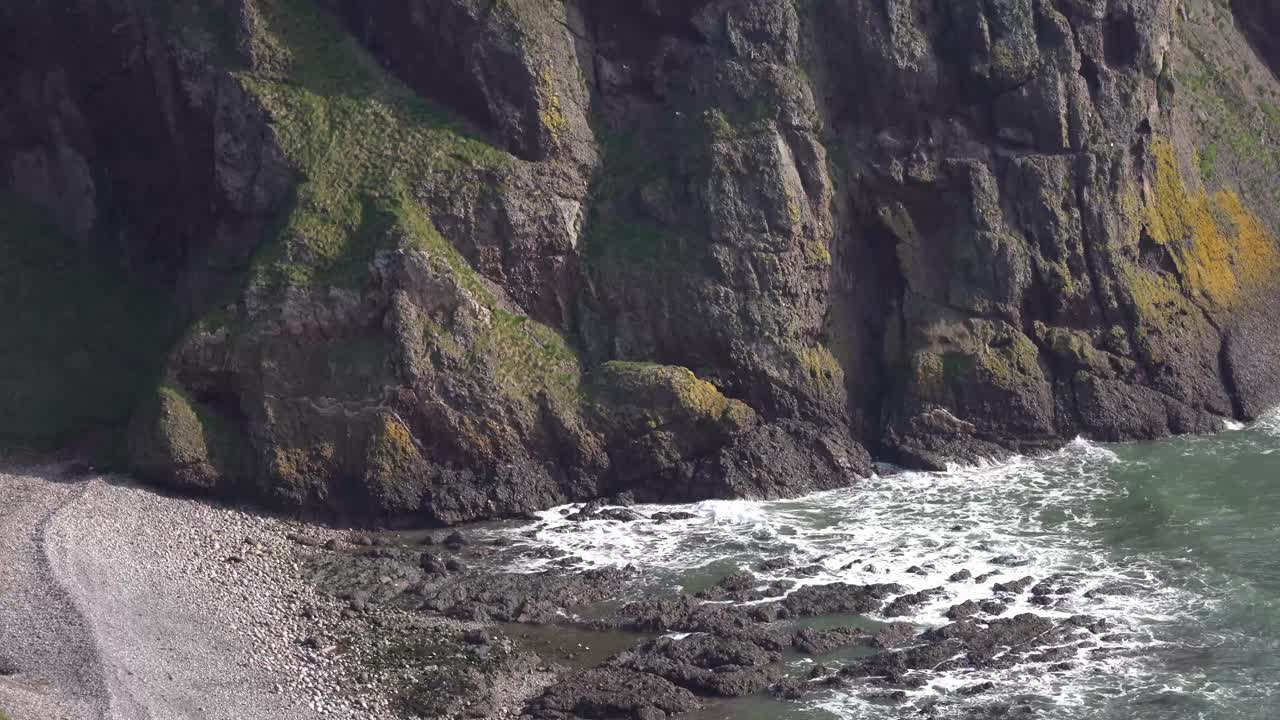 el castillo de dunnottar en el acantilado mientras la cámara se desplaza desde la playa y las olas se estrellan hacia la majestuosa fortaleza