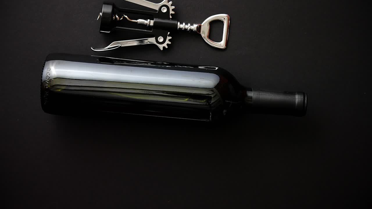 botella de vino tinto y sacacorchos sobre fondo negro mate