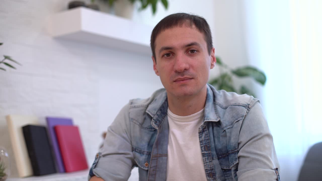 Giovane uomo studente scrittore, pensieroso e serio, seduto alla scrivania del suo ufficio di casa con il portatile, che cerca ispirazione e soluzioni a problemi, perso nei suoi pensieri, sognante, mentre guarda altrove