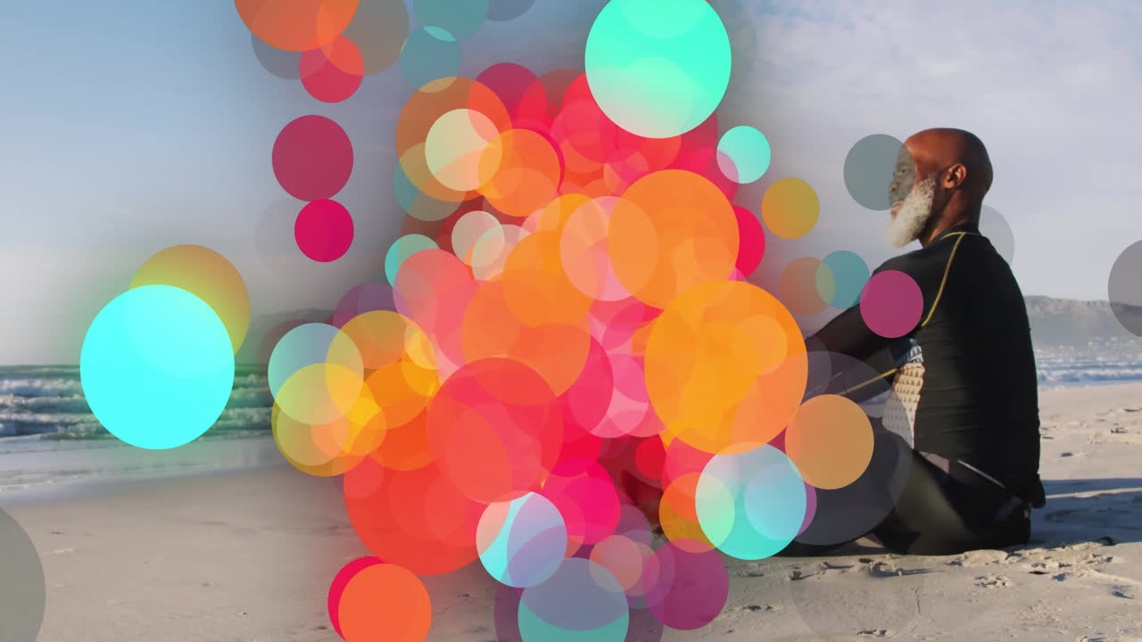Colorful circles animation over person sitting on sandy beach near ocean
