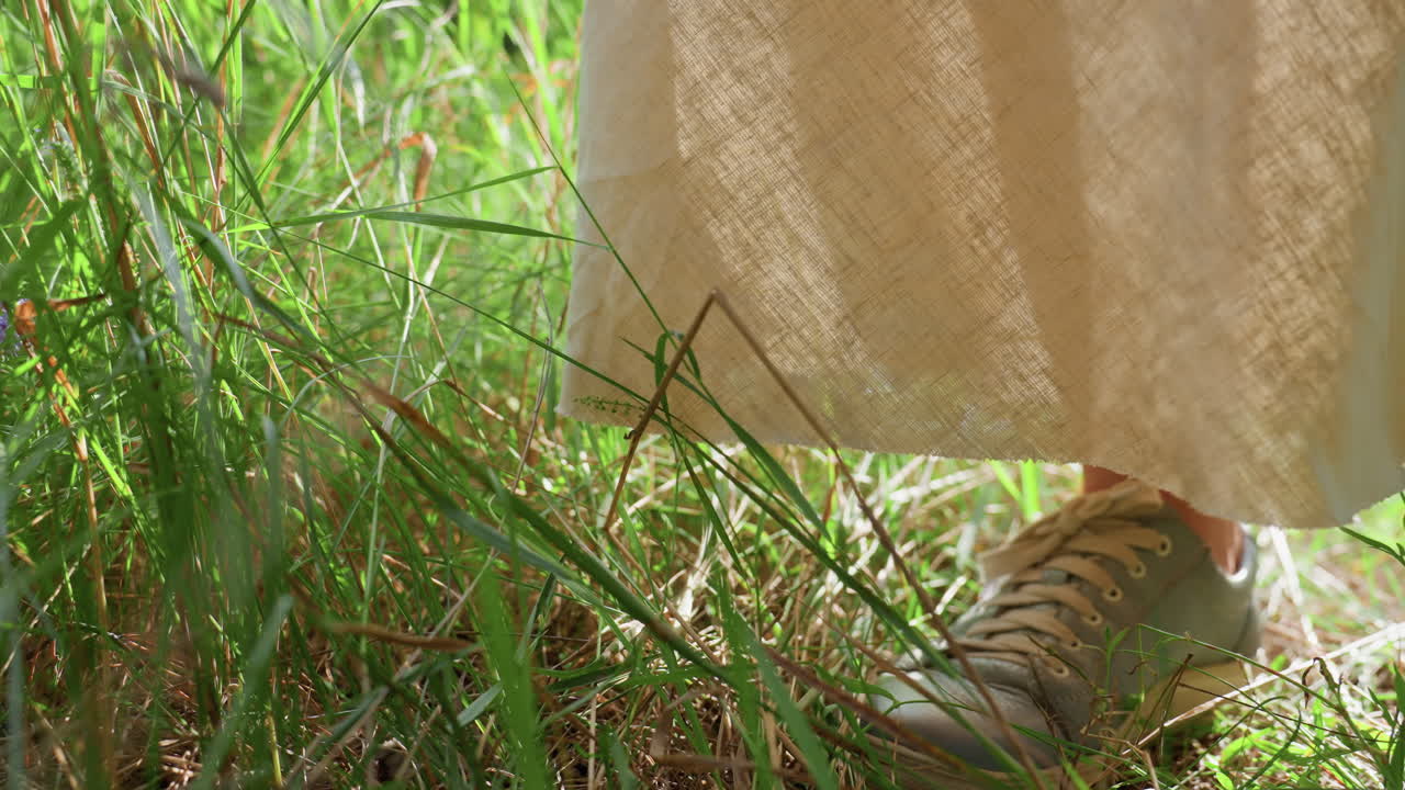 Leg view of woman wearing sneakers standing quietly on fresh green grass under sunlight, gentle breeze moving through blades, calm summer scene symbolizing freedom, simplicity, and connection