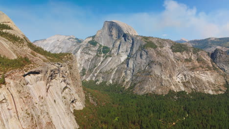 vertical rock formations lit with bright sun. pine tree wood growing at the foot of mountains in yosemite park, california, usa.