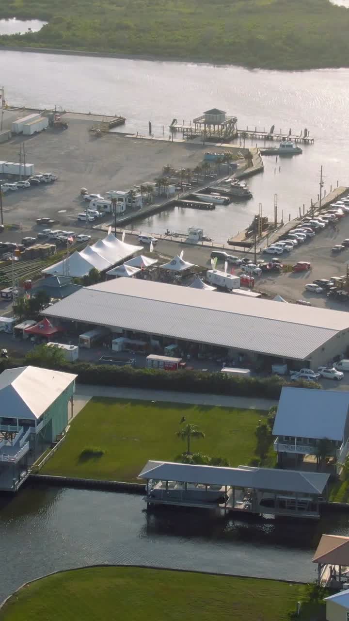 Vertical aerial footage of the Island Strong Festival on Grand Isle, Louisiana, featuring the marina, tents, traffic, arriving attendees, and sunlight reflecting off the bayou waters