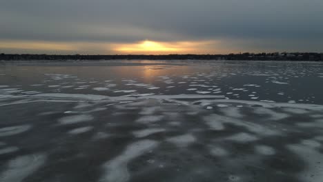frozen lake surface with different types of ice and snow on top during golden hour