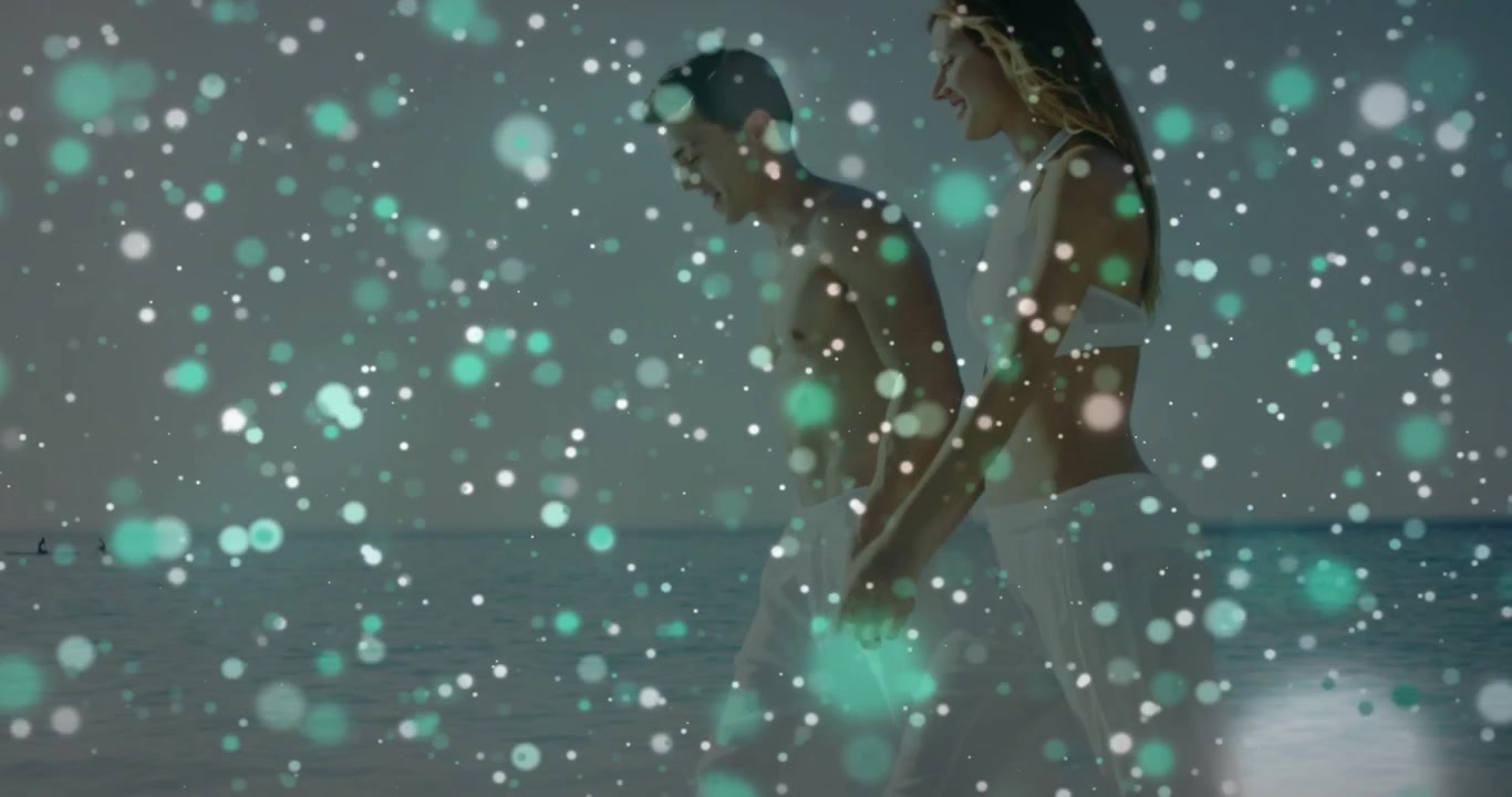 Uittrekkende opname onthult stel dat langs de kustlijn loopt in witte badkleding voor een fotoshoot, blauwgroen-witte bokeh.