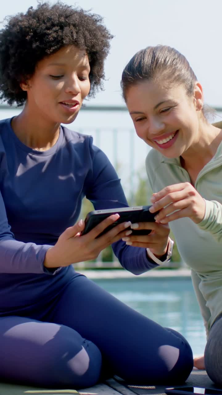 Vertical video: Laughing women in activewear leaning toward phone held nearby by pool sharing clip