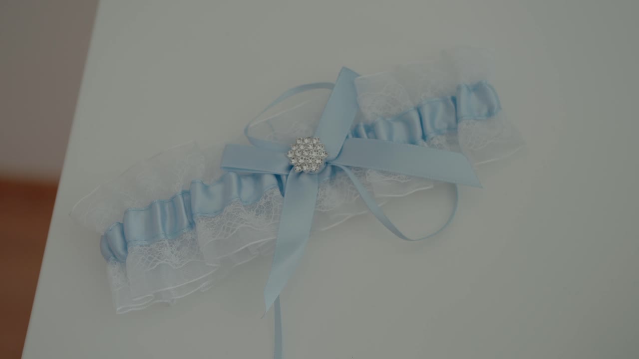 렌즈와 보석으로 된 활이 있는 섬세한 파란색 웨딩 가터가 부드러운  테이블에 놓여 있습니다.