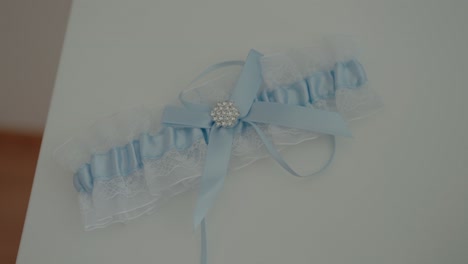 delicate blue wedding garter with lace and a jeweled bow rests on a smooth white table