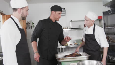 focused diverse male chef instructing trainee male chefs in kitchen, slow motion