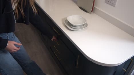 female model opening kitchen drawers and placing, putting in dinner plate, side plate and breakfast bowl and walking off in a modern kitchen