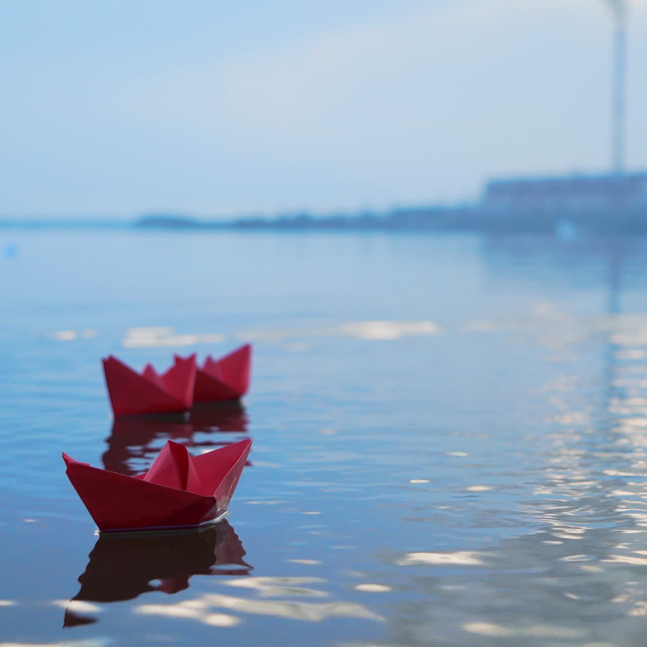 Childish paper boats floating on the water surface on the blurred background. Three red homemade ships on the river