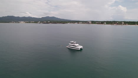 Drone-captures-a-yacht-with-a-half-orbit-side-shot-against-Careyeros-and-Punta-de-Mita,-Nayarit-coast-backdrop