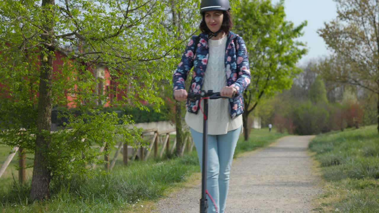 Giovane donna con il casco in sella a un monopattino elettrico su un sentiero di ghiaia, vista frontale