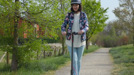 young woman with helmet rides electric scooter over gravel path, front