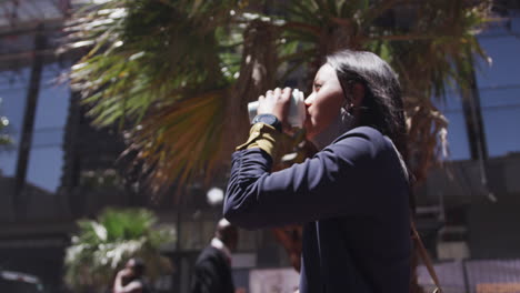 African-american-woman-wearing-face-mask-drinking-coffee-in-city-park