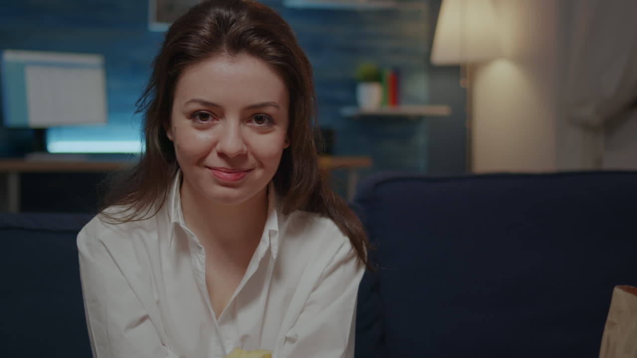Portrait of young woman holding bowl of chips sitting on sofa