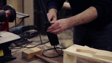 Un-Hombre-Irreconocible-Conecta-El-Equipo-A-La-Energía-Eléctrica,-Coloca-Su-Forma-En-El-Banco-Y-Comienza-A-Moler-El-Patrón-De-Forma-De-Pez-Con-Una-Máquina-Rectificadora.-Primer-Plano-Del-Hombre-Lijando-Madera-En-El-Taller.-Camara-Lenta