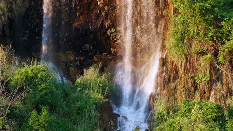 the natural waterfall that flows down the mountain is lit by the evening sun