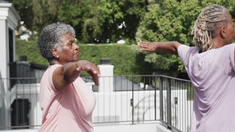 focused senior african american female friends practicing yoga standing on balcony, slow motion