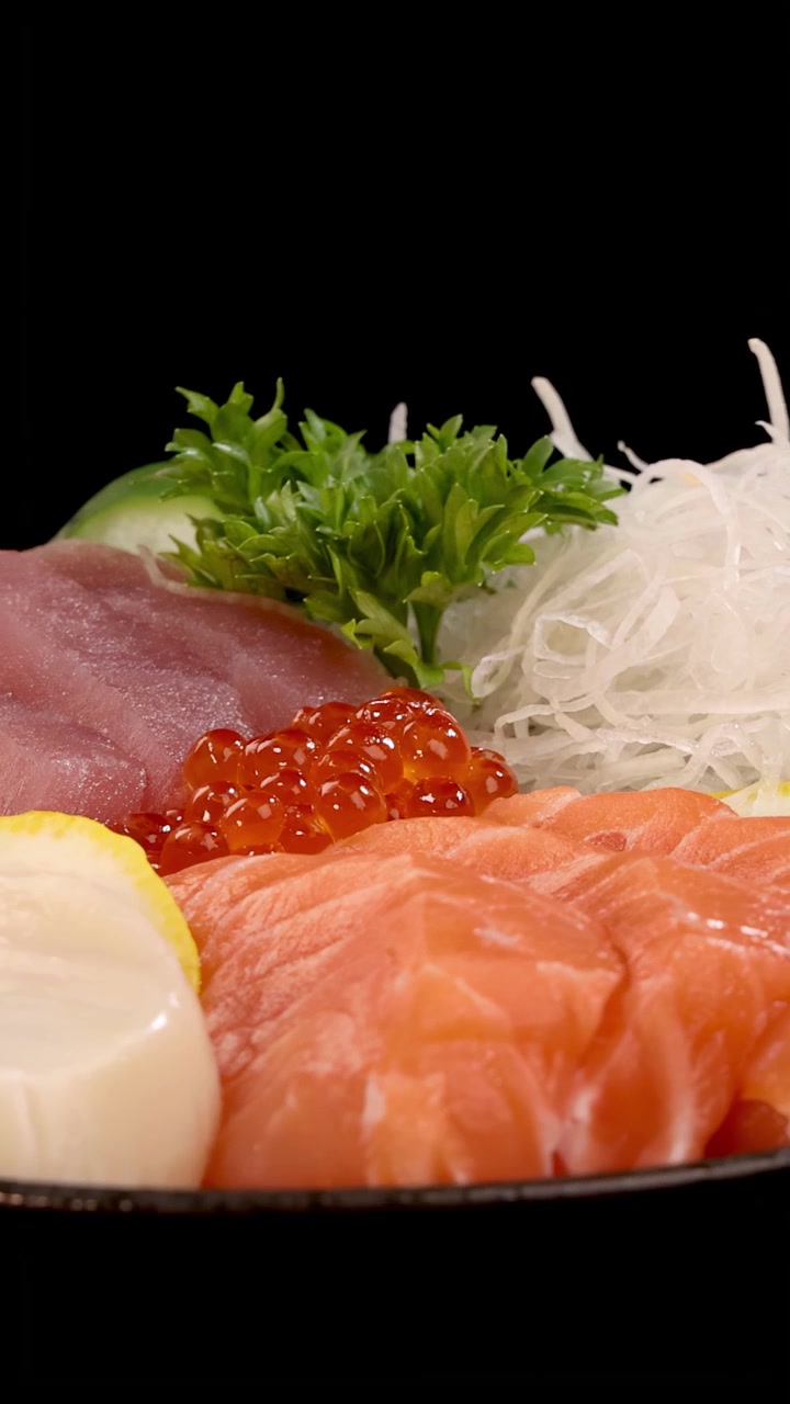 Sashimi e sushi assortiti, inclusi salmone, tonno, capasanta e uova di salmone, ruotano fluidamente sotto una brillante illuminazione da studio su uno sfondo nero senza soluzione di continuità.