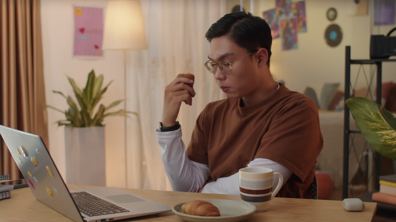 Gen Z Student Watching Online Webinar on Laptop and Eating Pastry