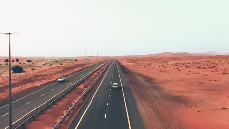 4k drone footage, a road between desert in sharjah, a car speeding on road, geological landscape of high dune desert in united arab emirates, drone videos