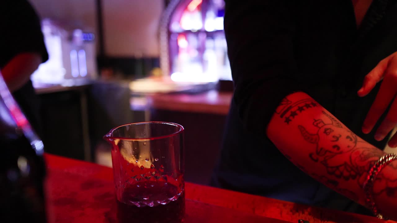 Bartender stirs cocktail with bar spoon under warm, moody lighting at a Bangkok bar counter