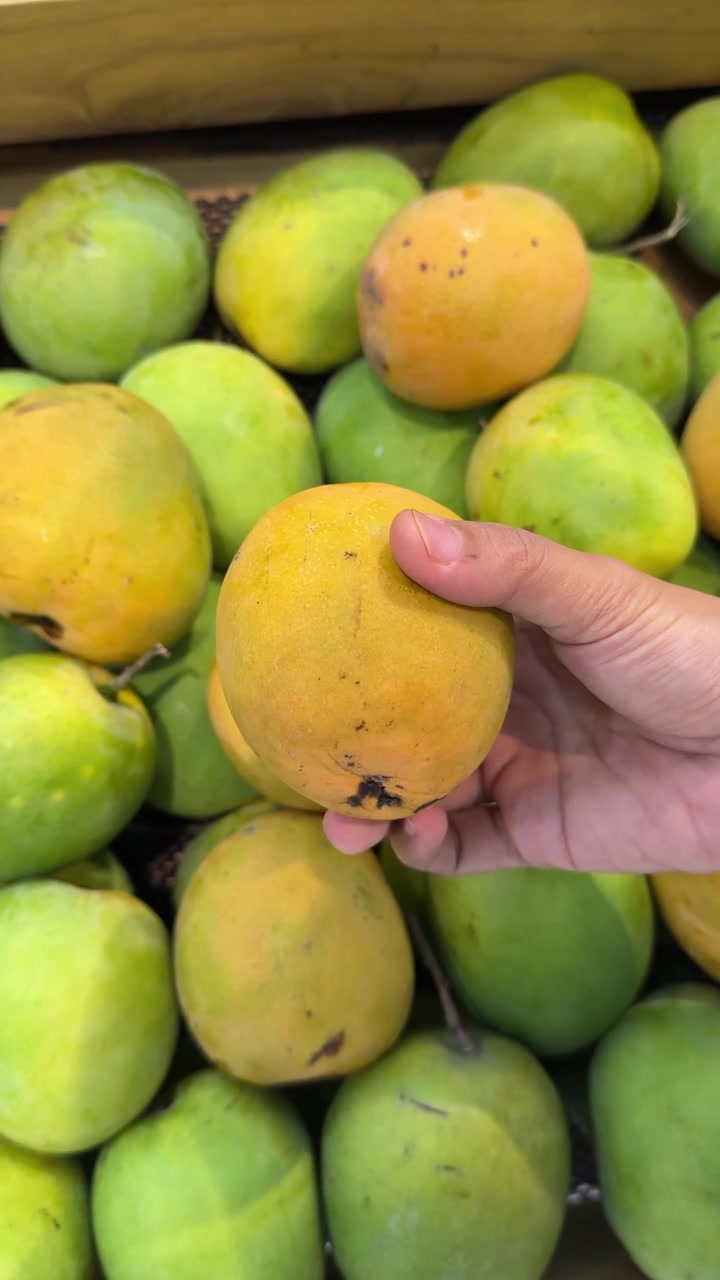 Ręczne wybieranie świeżych, dojrzałych mango w sklepie spożywczym