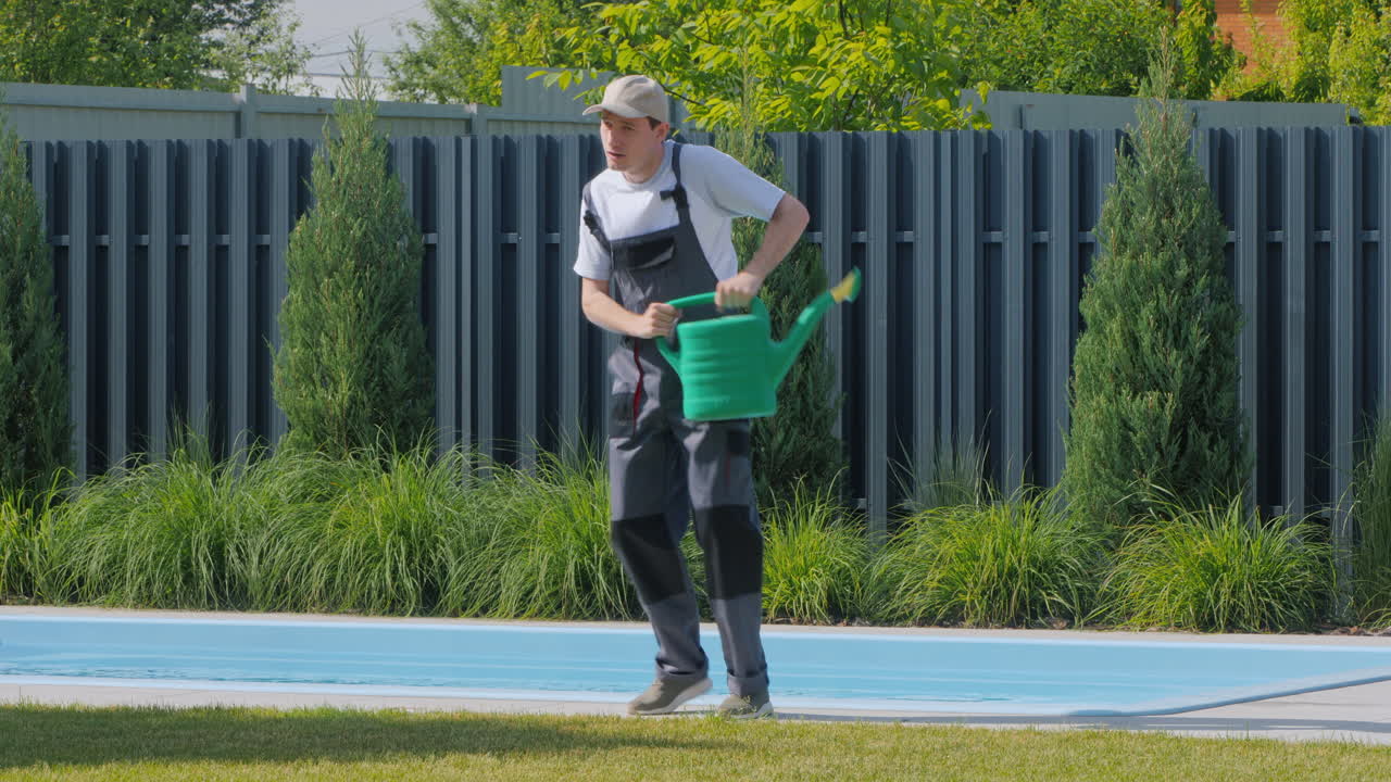 정원사 가 수영장 근처 에 있는 식물 들 에게 물 을 주고 있다