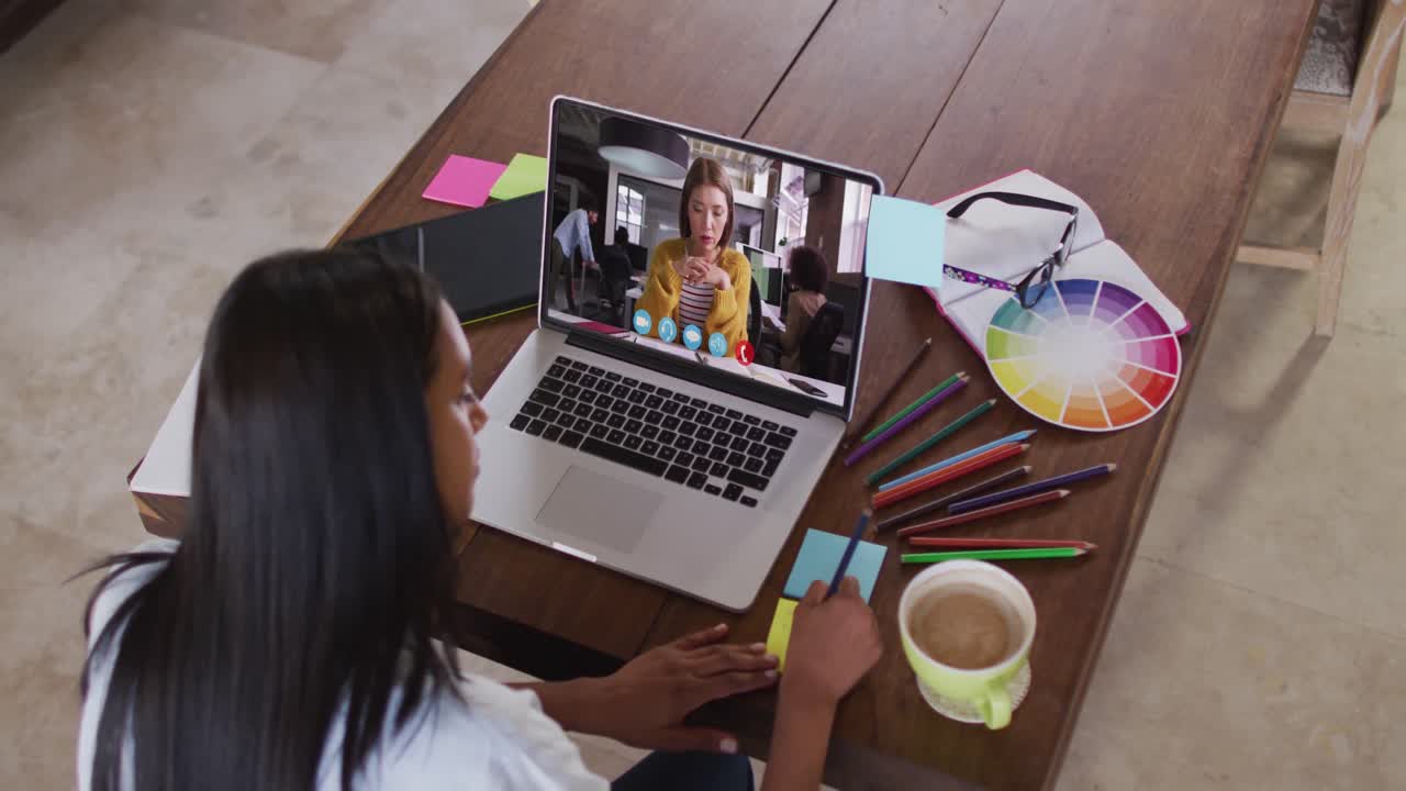 Mujer afroamericana escribiendo en notas adhesivas mientras realiza una videollamada en su computadora portátil en casa.