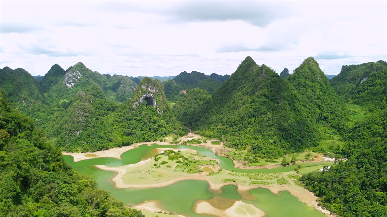 Tomada aérea de drone mostrando o buraco único da montanha Nui Mat Than, cercada por exuberantes picos cársticos verdes e um rio turquesa sinuoso no vale de Cao Bang.