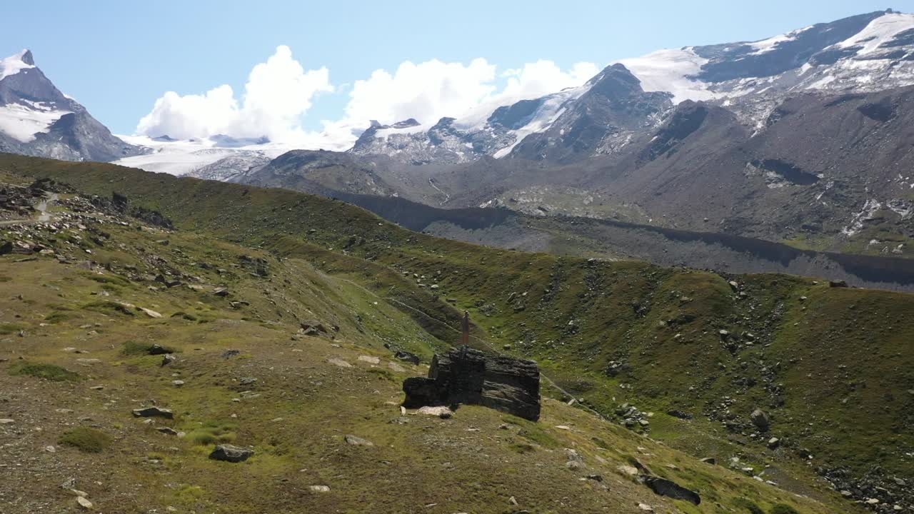 amplia toma aérea que circula alrededor de un joven solo en una gran roca, de pie en lo alto para ver la vista del valle de matterhorn