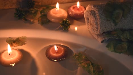 relaxing spa background with candles floating in the bath water, some green petals and a towel near the water surface