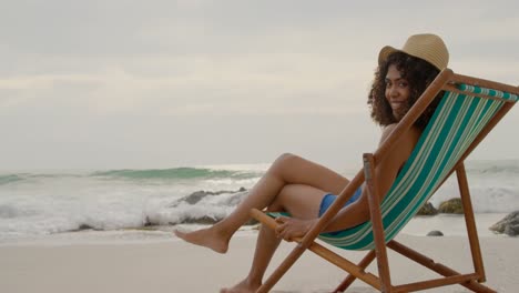 vista lateral de una mujer afroamericana relajándose en una tumbona en la playa 4k