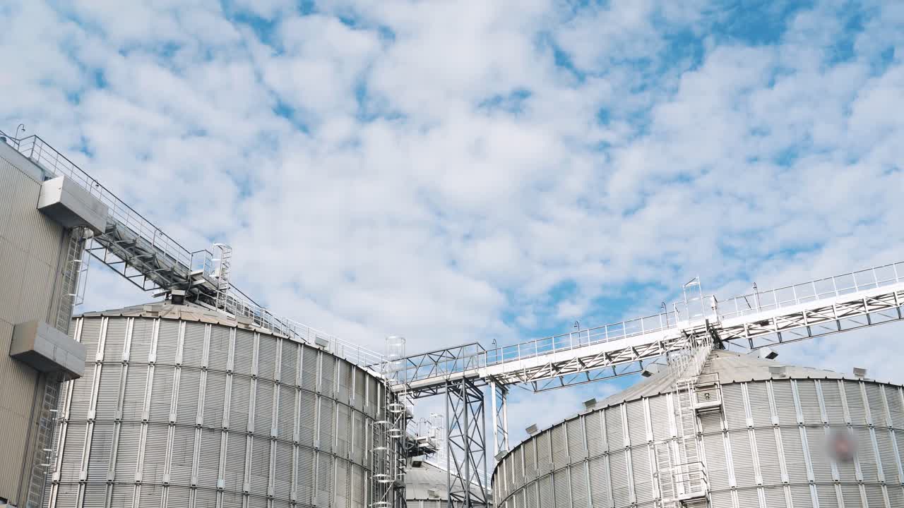 Modern agricultural complex in sunny day. Harmful smoke from grain dryer. Large silver silos for grain processing. Nature in danger