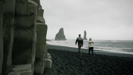 couple walking on black sand beach in iceland