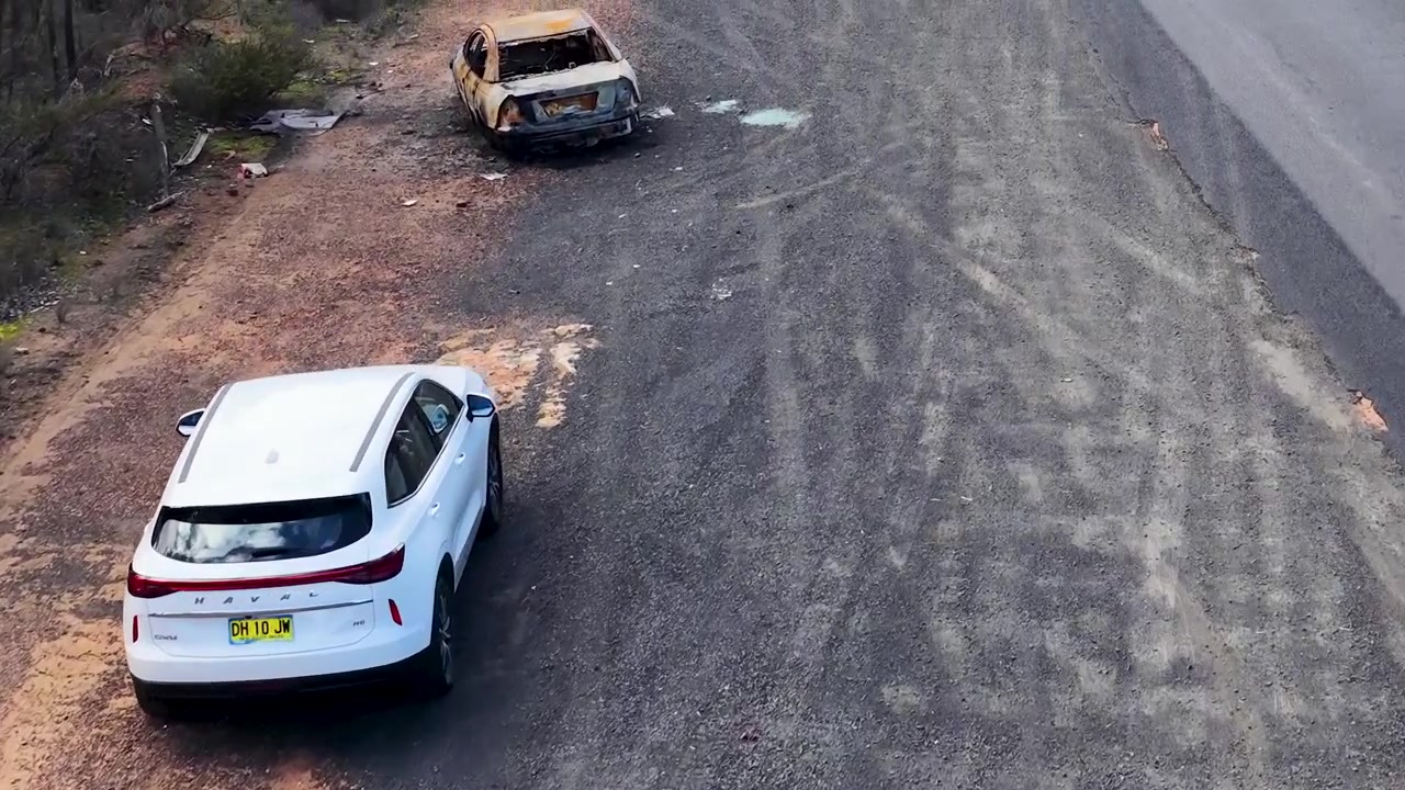Luchtfoto van een wit voertuig dat langs een verlaten, uitgebrand autowrak rijdt in Australië