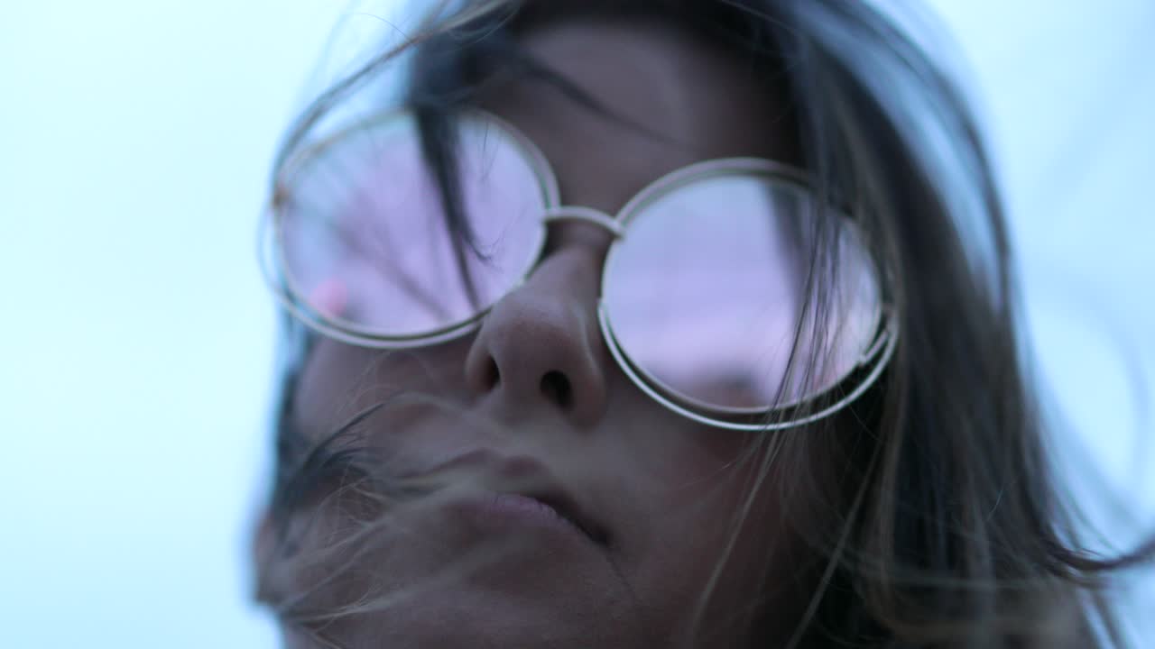 una chica con unas gafas de sol grandes y redondas, con el pelo soplado por el viento.