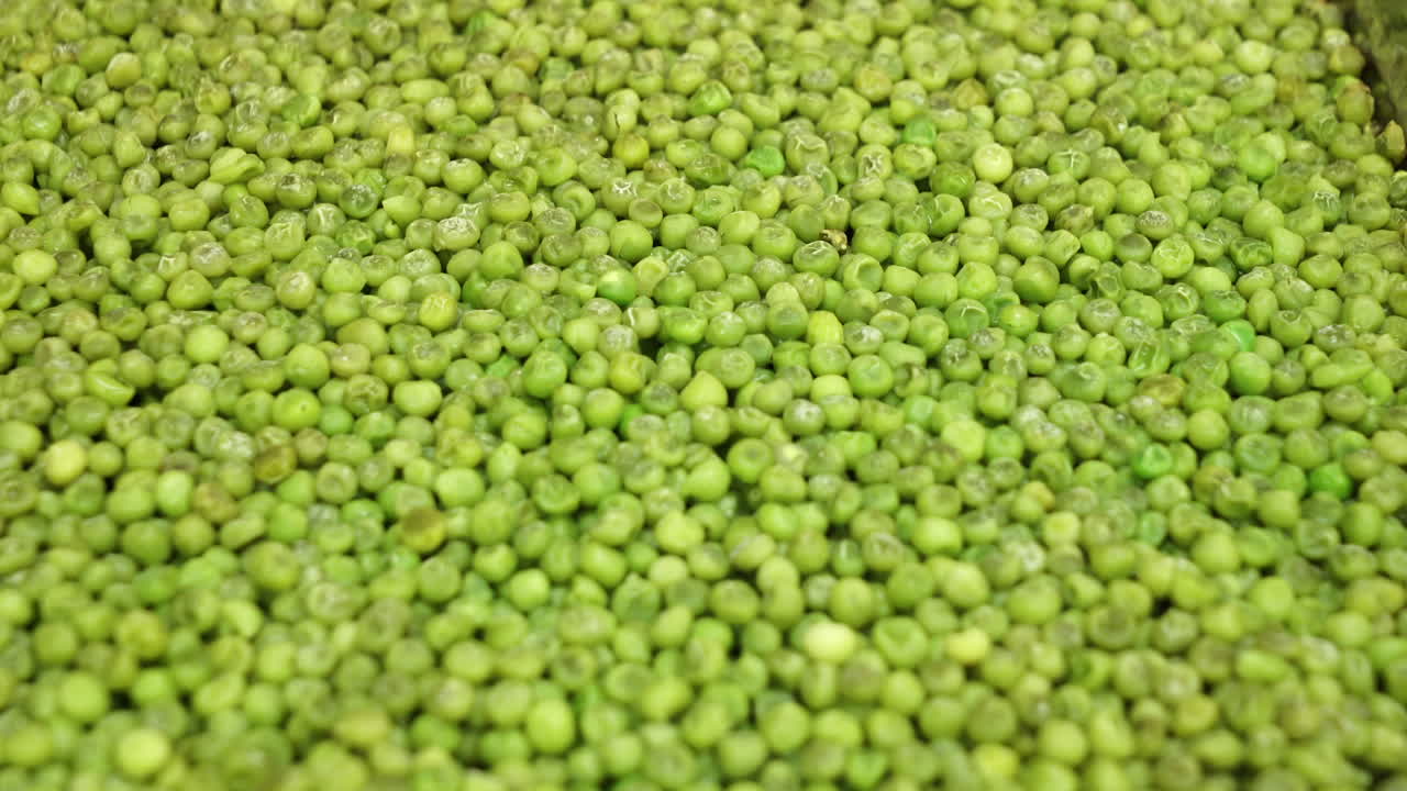 primer plano de guisantes verdes cocinados en una bandeja de metal de una cocina industrial
